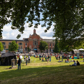 Families and people of different ages gather on a grassy lawn infront of a stately building.