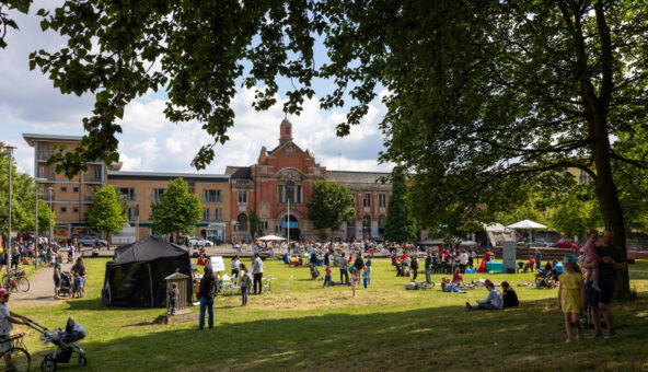 Families and people of different ages gather on a grassy lawn infront of a stately building.