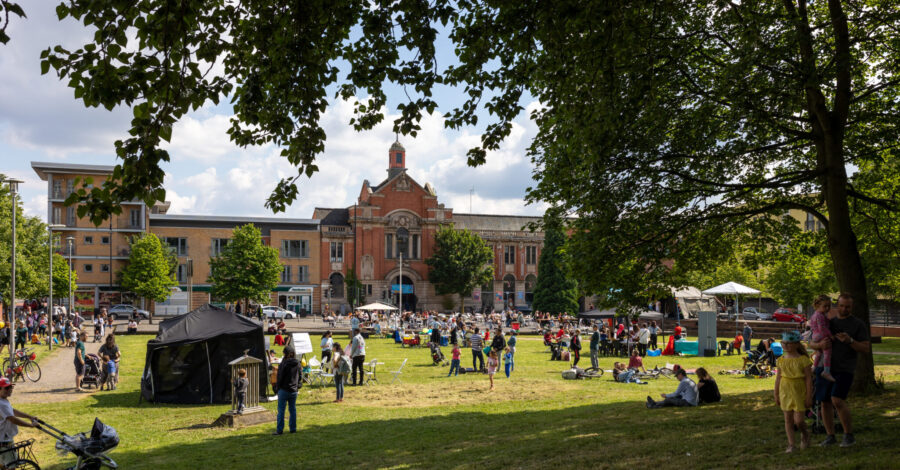 Families and people of different ages gather on a grassy lawn infront of a stately building.