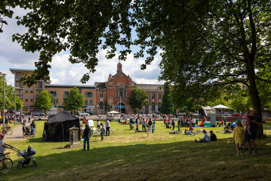 Families and people of different ages gather on a grassy lawn infront of a stately building.