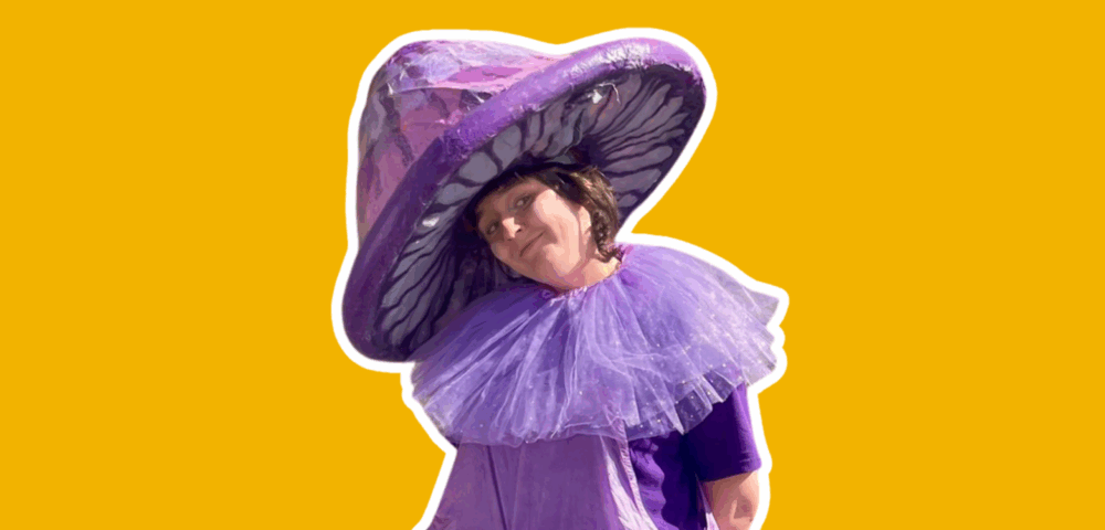 A performer dressed as a giant purple mushroom, with a purple hat and a purple ruff.