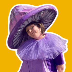 A performer dressed as a giant purple mushroom, with a purple hat and a purple ruff.