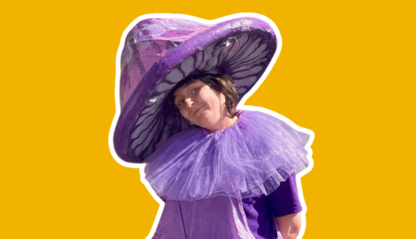 A performer dressed as a giant purple mushroom, with a purple hat and a purple ruff.