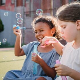 Two young girls sat down on the grass blowing bubbles.