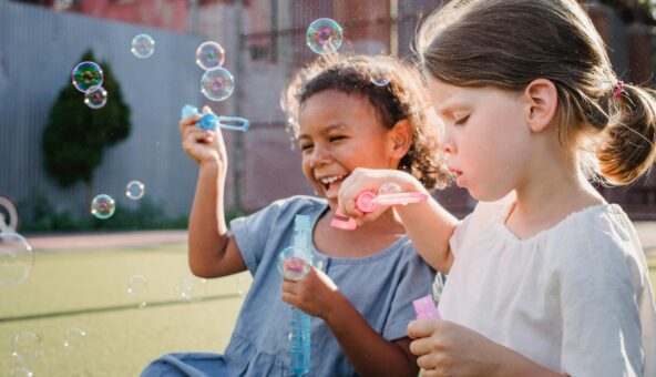 Two young girls sat down on the grass blowing bubbles.