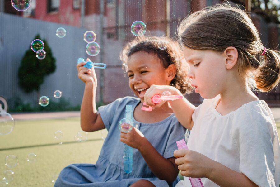 Two young girls sat down on the grass blowing bubbles.