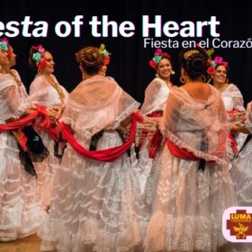 A group of female Mexican dancers in traditional dress of long full-skirted white dresses made of lace, red scarfs and flowers in their hair.