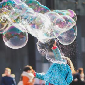 A girl in a blue cardigan creating a huge string of bubbles