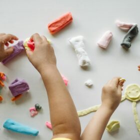 Children playing with different coloured clay on a white tabletop.