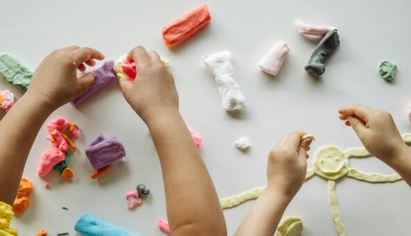 Children playing with different coloured clay on a white tabletop.