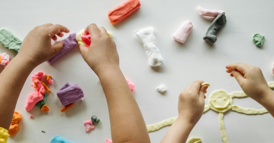 Children playing with different coloured clay on a white tabletop.