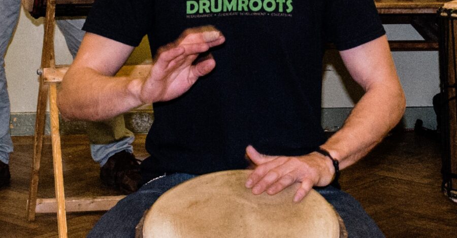A person wearing a black 'Drumroots' t-shirt playing a drum.