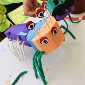 A creature that looks like an insect that has been crafted from coloured paper, cardboard with pipecleaners for legs.