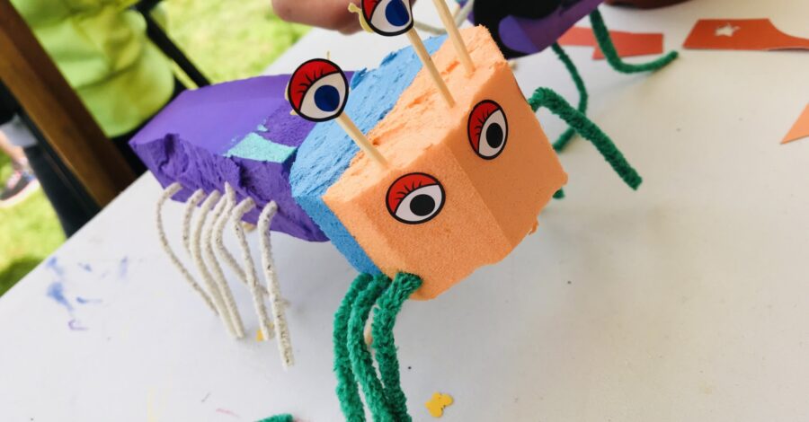 A creature that looks like an insect that has been crafted from coloured paper, cardboard with pipecleaners for legs.