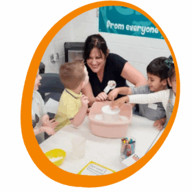 An adult sat at a table with two children doing an activity.