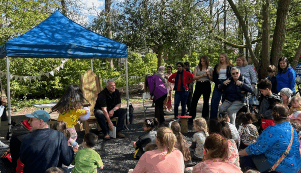 A blue gazebo and a number of families and people sat on the floor and stood up ready for a storytelling event.
