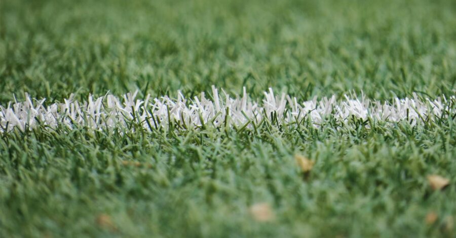 A close up of the green grass on a football pitch with a white line sprayed onto it.