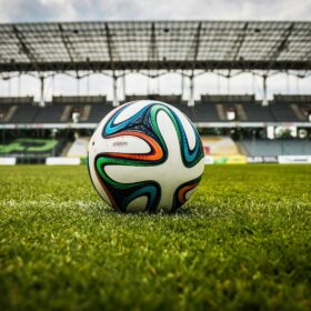A multi-coloured football on the middle of the pitch in a football stadium.