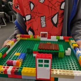 A child holding their Lego creation, which looks like a half built house.