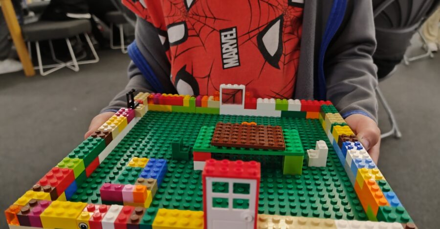 A child holding their Lego creation, which looks like a half built house.