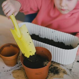 A child using a yellow trowel to put soil into plant pots.