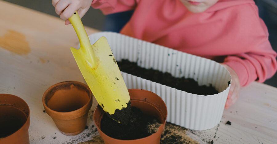 A child using a yellow trowel to put soil into plant pots.