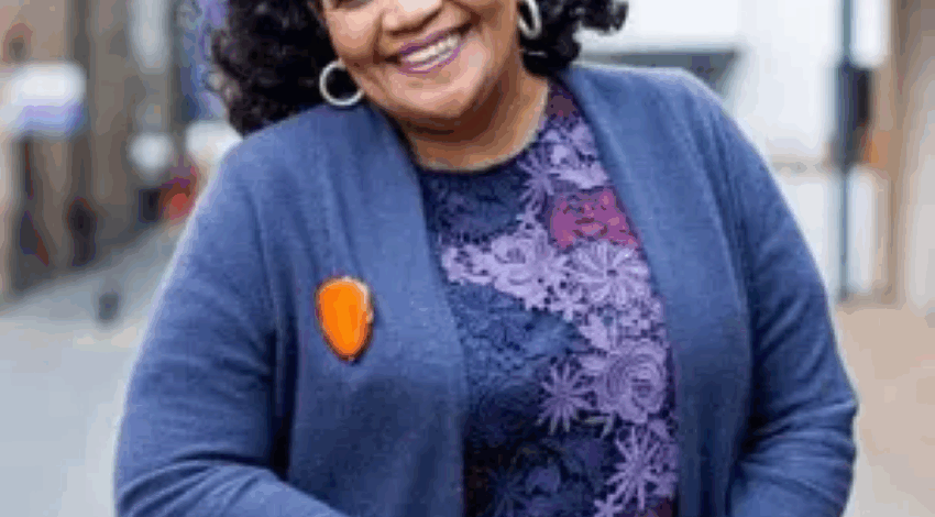 Poet Lorna Goodison smiling and leaning on a brick wall outside.