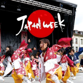 Japanese dancers performing on a stage with a backdrop that reads 'Japan Week'.