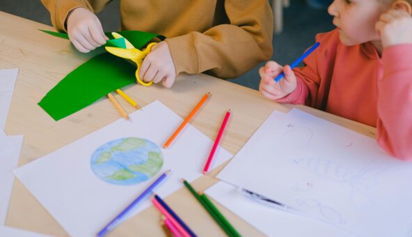 Children taking part in a craft activity that involves colouring in and cutting paper.