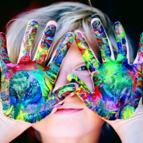 boy with brightly painted hands in front of face