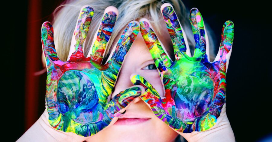 boy with brightly painted hands in front of face