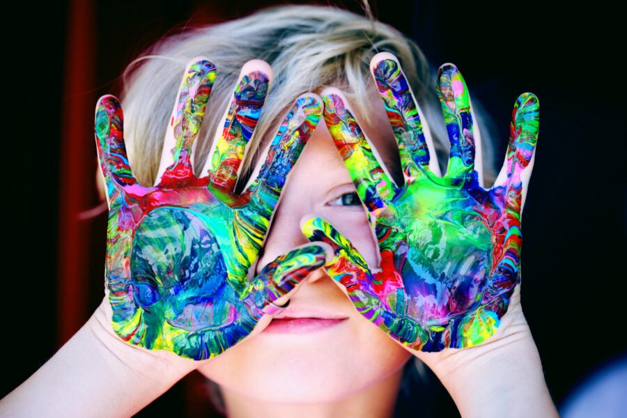 boy with brightly painted hands in front of face