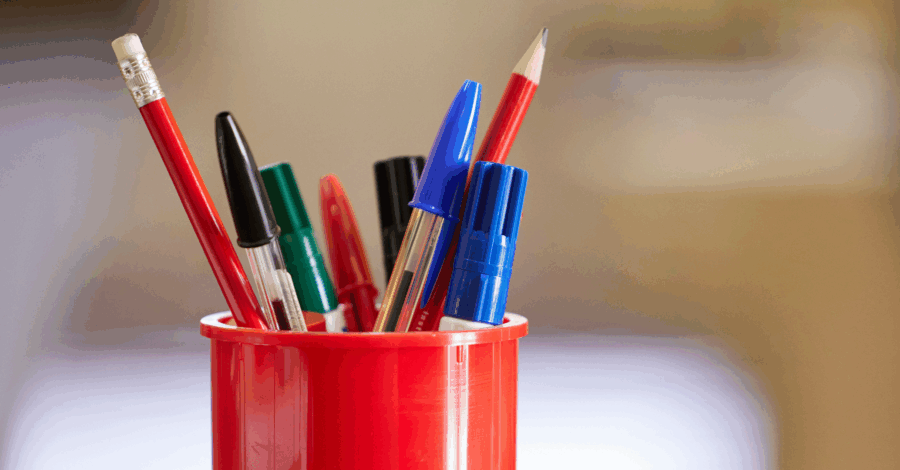A red plastic container full of different coloured pens.