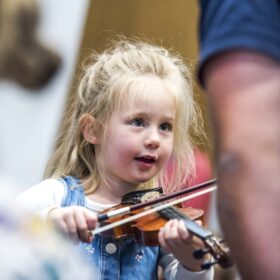 A small child holds a violin underneath their chin and presses a bow on the strings.