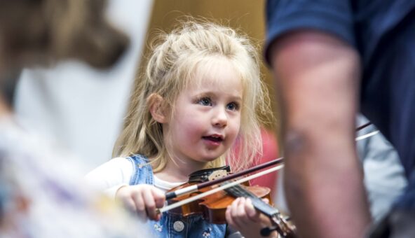 A small child holds a violin underneath their chin and presses a bow on the strings.