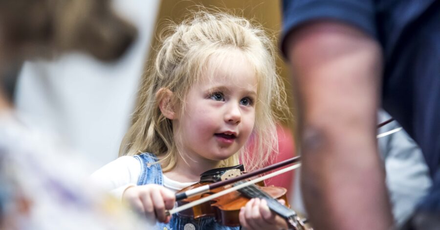 A small child holds a violin underneath their chin and presses a bow on the strings.