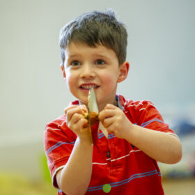 A small child wearing a red shirt, playing a tiny cymbal.