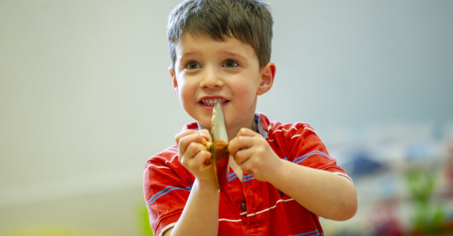 A small child wearing a red shirt, playing a tiny cymbal.