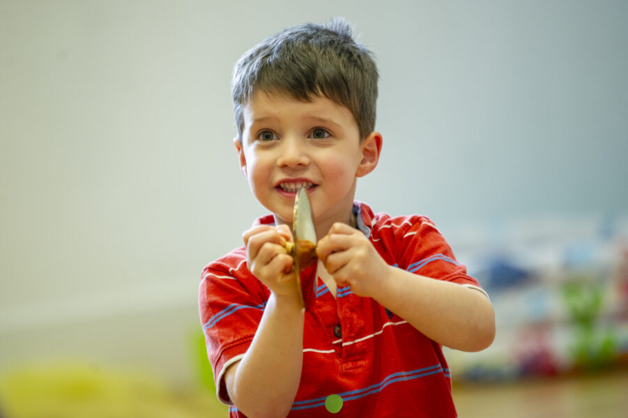 A small child wearing a red shirt, playing a tiny cymbal.