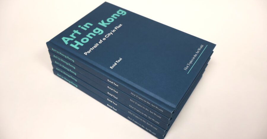 A stack of six hardcover books with dark blue covers titled Art in Hong Kong: Portrait of a City in Flux by Enid Tsui. The text on the cover and spine is printed in teal and white. The books are neatly stacked on a light-colored surface.
