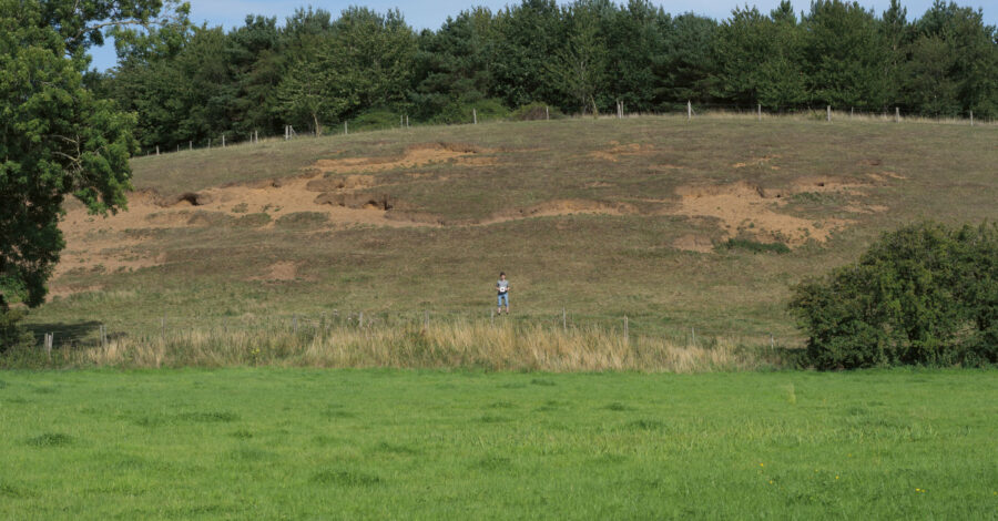 A view across a field with a hill in the background. A person stands in the distance.