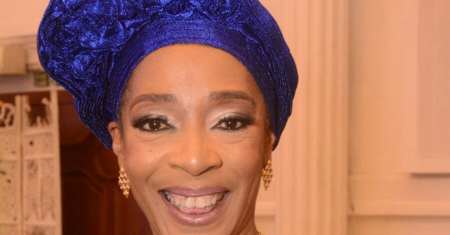 Erinma Bell, anti-gun and gang crime campaigner and activity. She is smiling and wears a ble headress, gold earrings and a gold necklance.