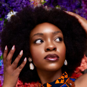 A woman with afro hair in front of a floral background.
