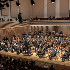 A symphony orchestra of young people performing at the Stoller Hall, with audience.