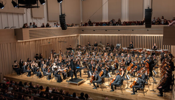 A symphony orchestra of young people performing at the Stoller Hall, with audience.