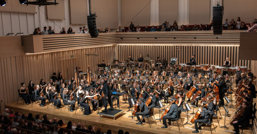 A symphony orchestra of young people performing at the Stoller Hall, with audience.
