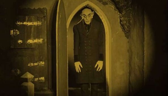 A black and white still of a man with distorted features walking through an arched doorway