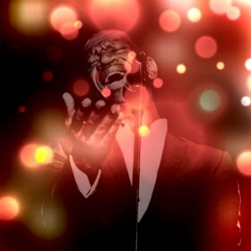 A gospel singer performing with different coloured Christmas lights around him.