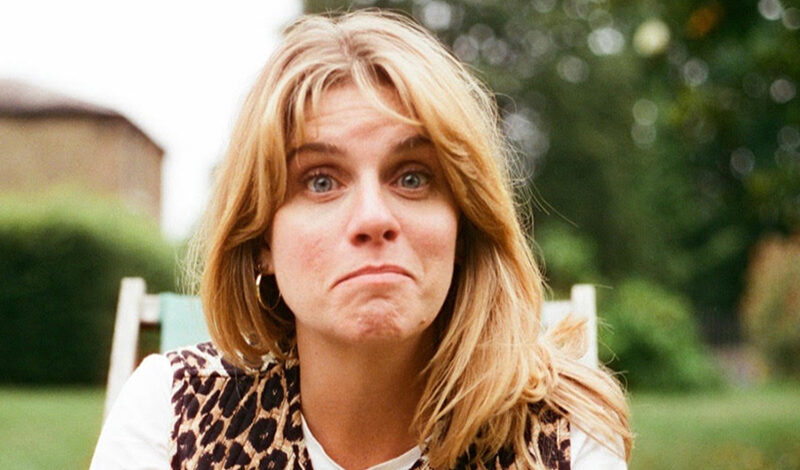 Writer Georgie Jones sat outside on a white chair pulling a confused and intriguing face.