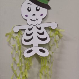 A skeleton made out of paper, wearing a black, green and red hat.